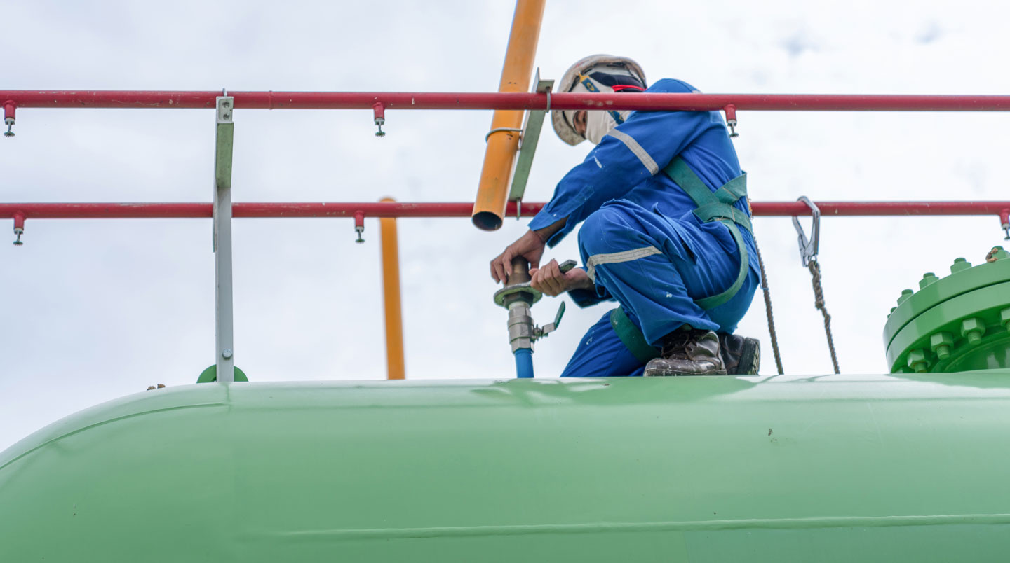 Technicien certifié en vêtement haute visibilité effectuant contrôle technique réglementaire sur vanne de citerne de propane avec outils de mesure professionnels